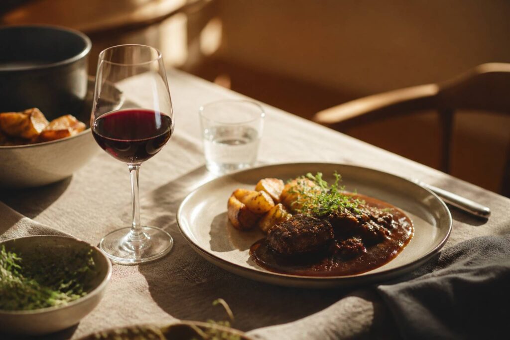 Verre de vin rouge posé près d'une assiette de viande en sauce